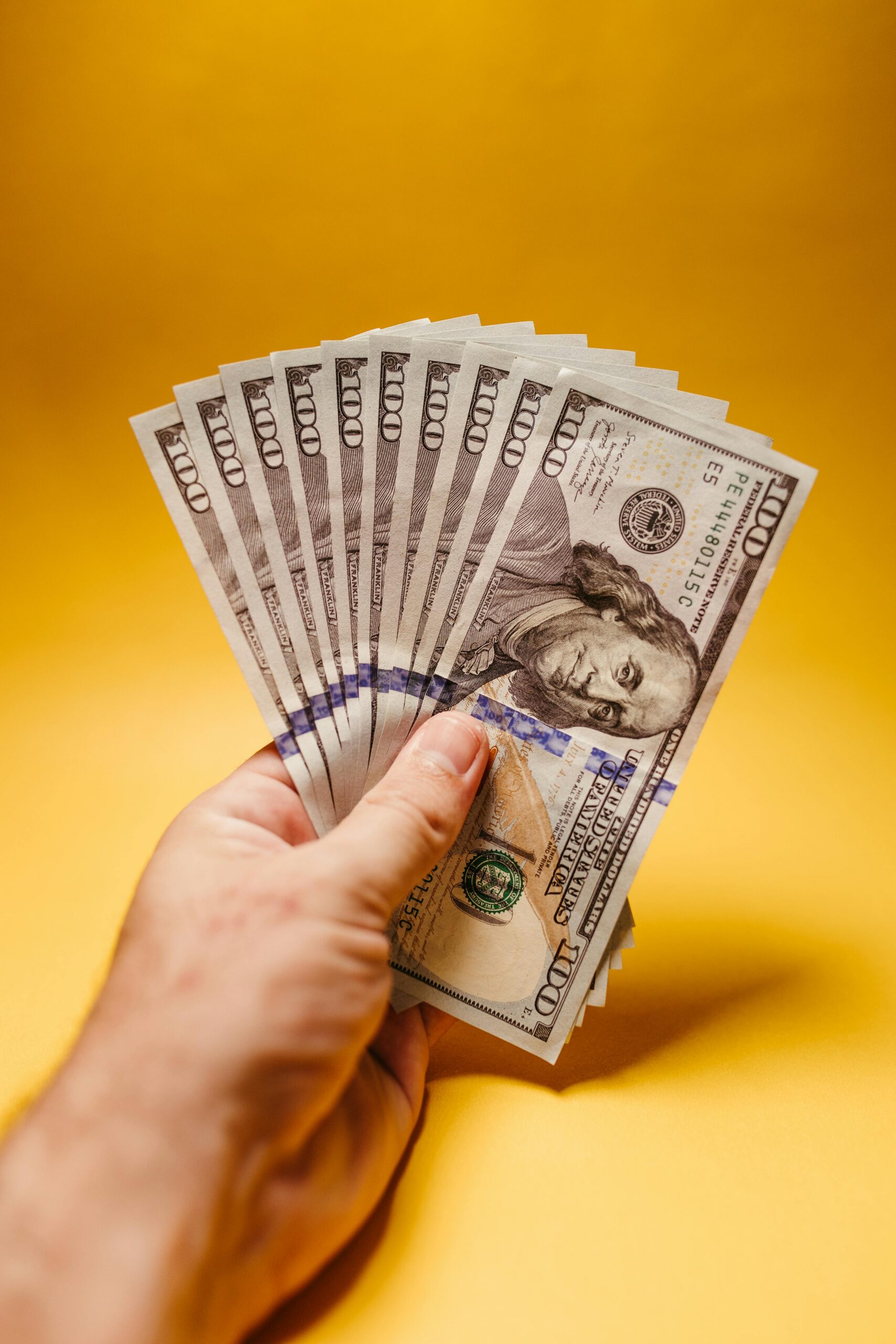Close-up of a hand displaying US dollar bills against a bright yellow backdrop, signifying wealth and finance.